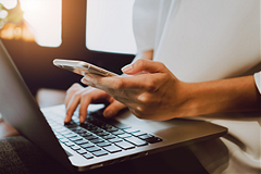 photo of a person using a smartphone while working on a laptop keyboard